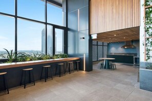 A modern bar area with high windows, a kitchen, and a seating area with stools.