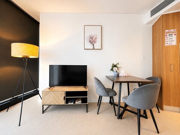 Ein modernes Zimmer mit Fernseher, Esstisch mit Stühlen, Lampe und einem gerahmten Bild an der Wand.
