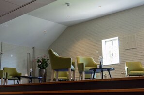 Relax in a spacious room with a high ceiling, featuring a seating area with green chairs and a wall-mounted screen.