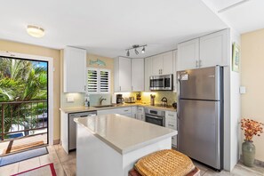A modern kitchen with white cabinets, stainless steel appliances, and a central island. - Kihei Beach #210 – Oceanfront Gem with A/C, Lanai, Pool and Sugar Beach Access (Kihei, Maui)