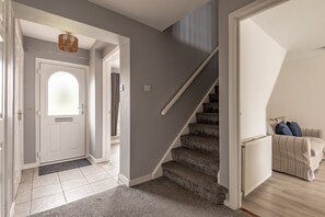 A hallway with a white door, a staircase, and a striped sofa in the background.