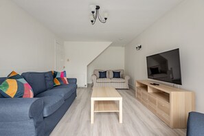 A modern living room with a sofa, coffee table, TV stand, and a staircase leading to another room.