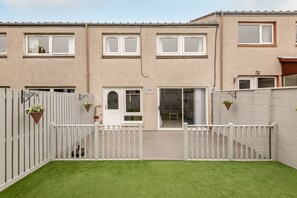 A residential building with a gated entrance, a small lawn, and a sliding glass door leading to a covered patio.