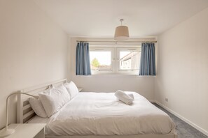 A bedroom with a bed, a nightstand, a window with curtains, and a hanging light fixture.