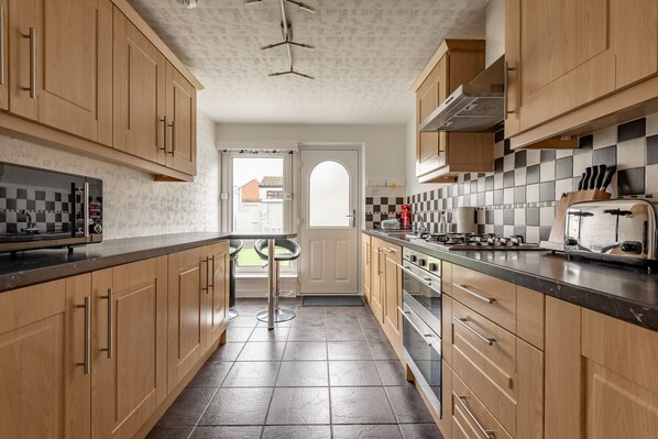 A kitchen with wooden cabinets, a black countertop, a refrigerator, a stove, and a toaster.