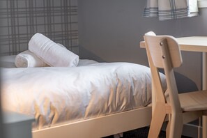 A neatly made bed with a rolled white towel, a wooden chair, and a small table in a hotel room. - Fraser Avenue (No 16) (St Andrews)