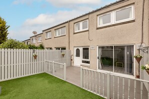 A row of terraced houses with a white picket fence, a small garden with artificial grass, and a balcony with a white railing. - Fraser Avenue (No 16) (St Andrews)