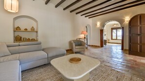 A spacious living area with a sofa, armchair, and a coffee table, featuring exposed wooden beams and a tiled floor.