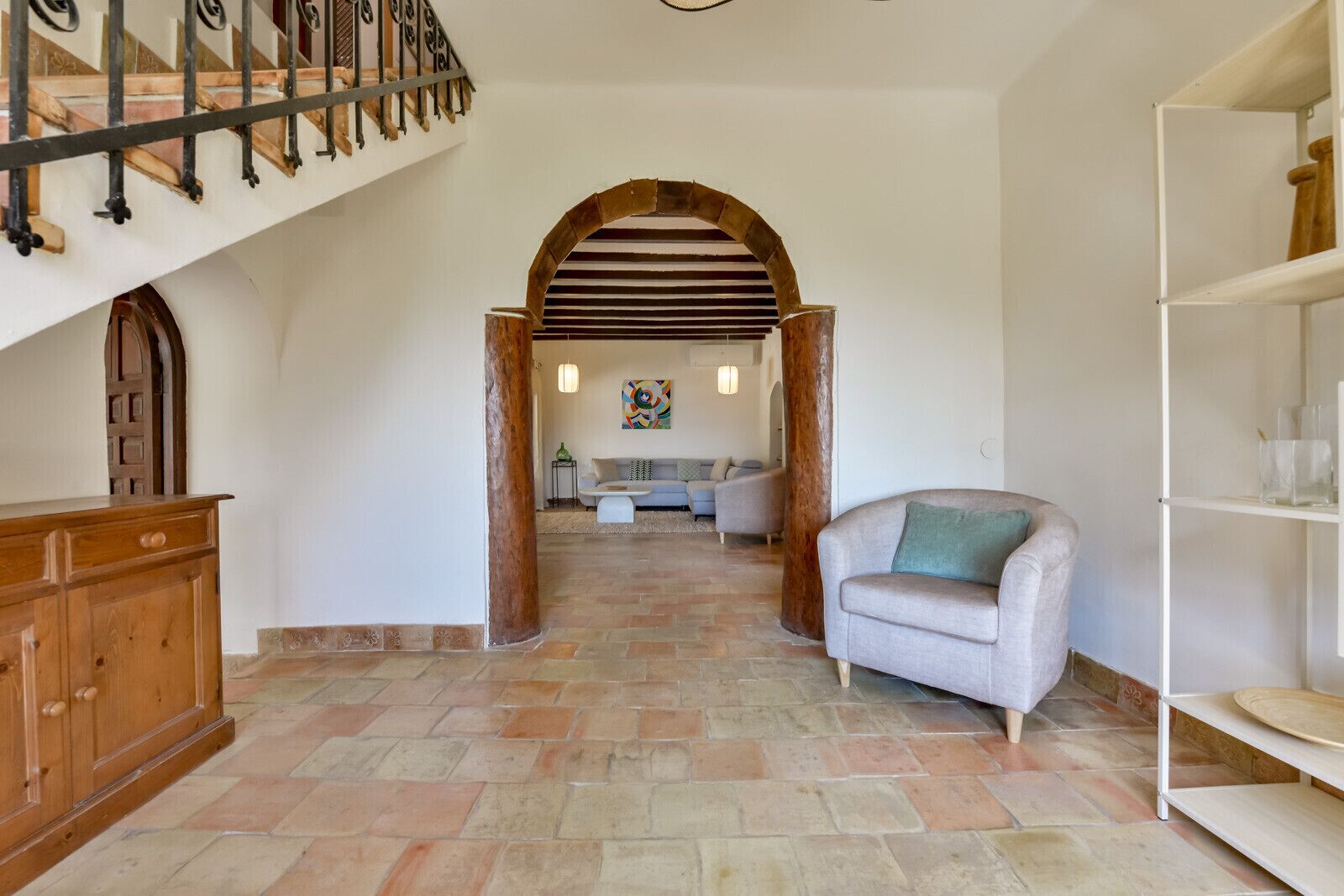 A spacious living area with a staircase, a wooden cabinet, a sofa, and a bookshelf.