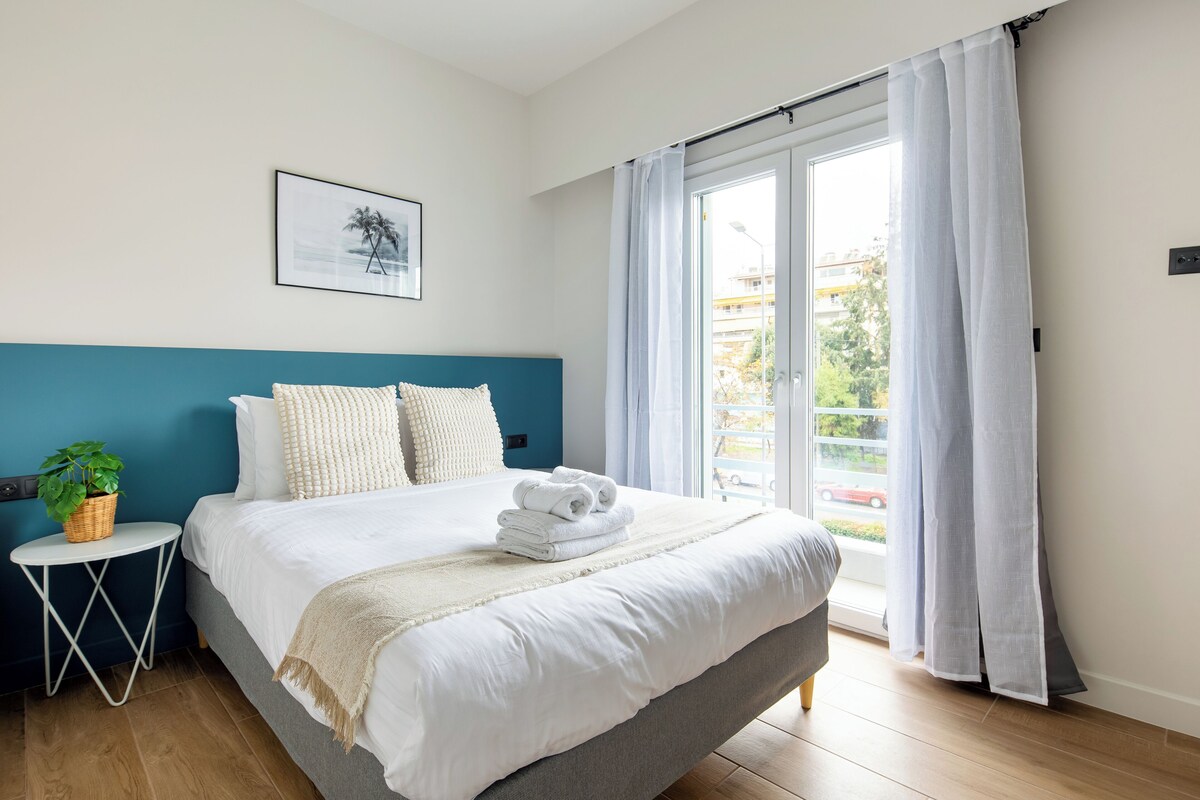 A bedroom with a bed, a small side table with a plant, and a window with curtains.