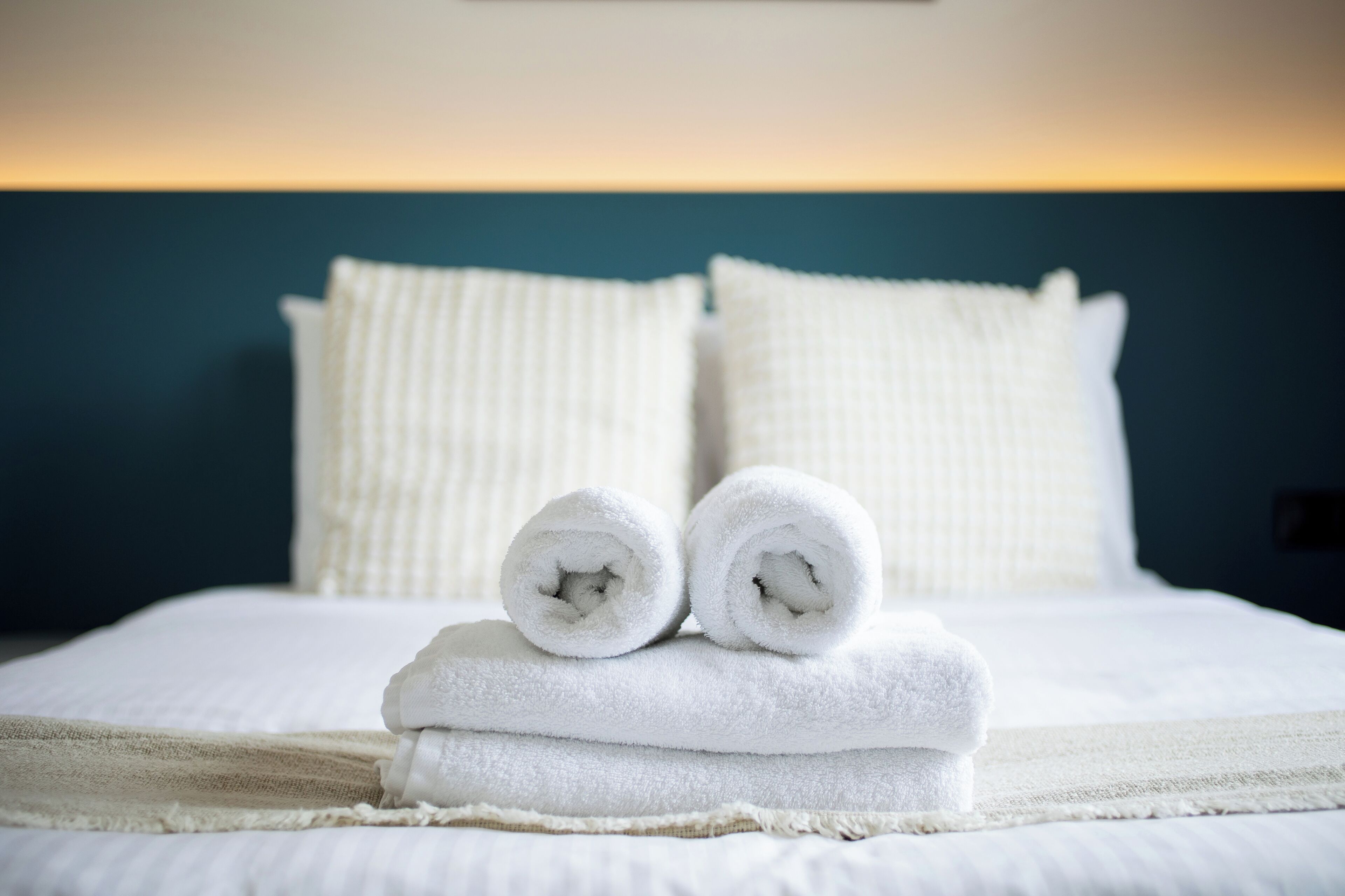 A neatly made bed with rolled white towels and a beige throw blanket.