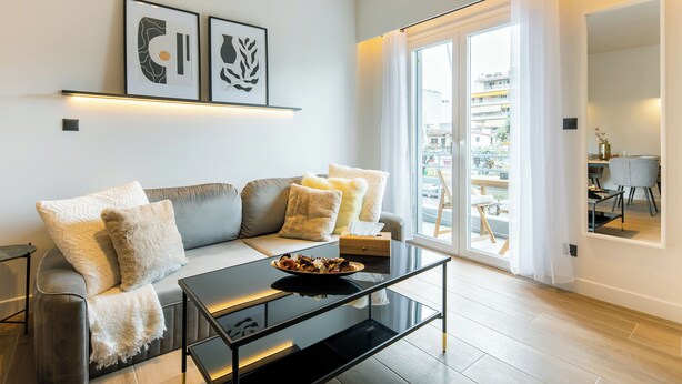 Una sala de estar moderna con un sofá, una mesa de centro de vidrio y vistas al exterior a través de un amplio ventanal corredero.
