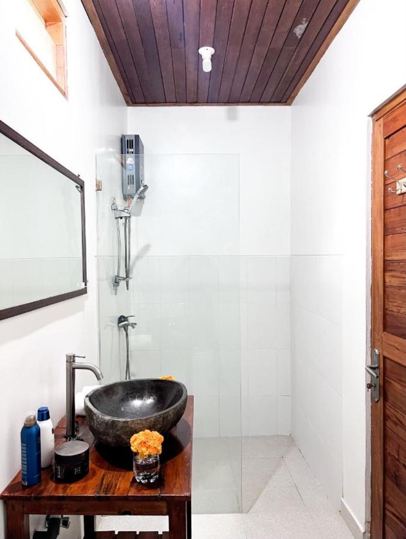 A bathroom with a wooden vanity, a large black basin, a mirror, a shower, and a wooden door.