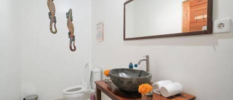 A bathroom with a wooden vanity, a large mirror, a vessel sink, and decorative wall hooks.
