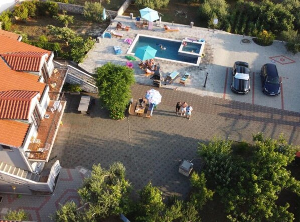 Vista aérea de una zona residencial con piscina, mobiliario exterior y coches aparcados.