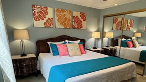 Ein Hotelzimmer mit einem großen Bett, zwei Nachttischen mit Lampen, einem Spiegel und floralen Bildern an den Wänden.