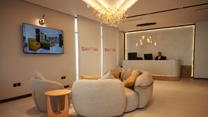 A modern hotel lobby with a reception desk, a large screen displaying a room, and comfortable seating areas. - Palm Core Hotel Al Rabwah (Riyadh)