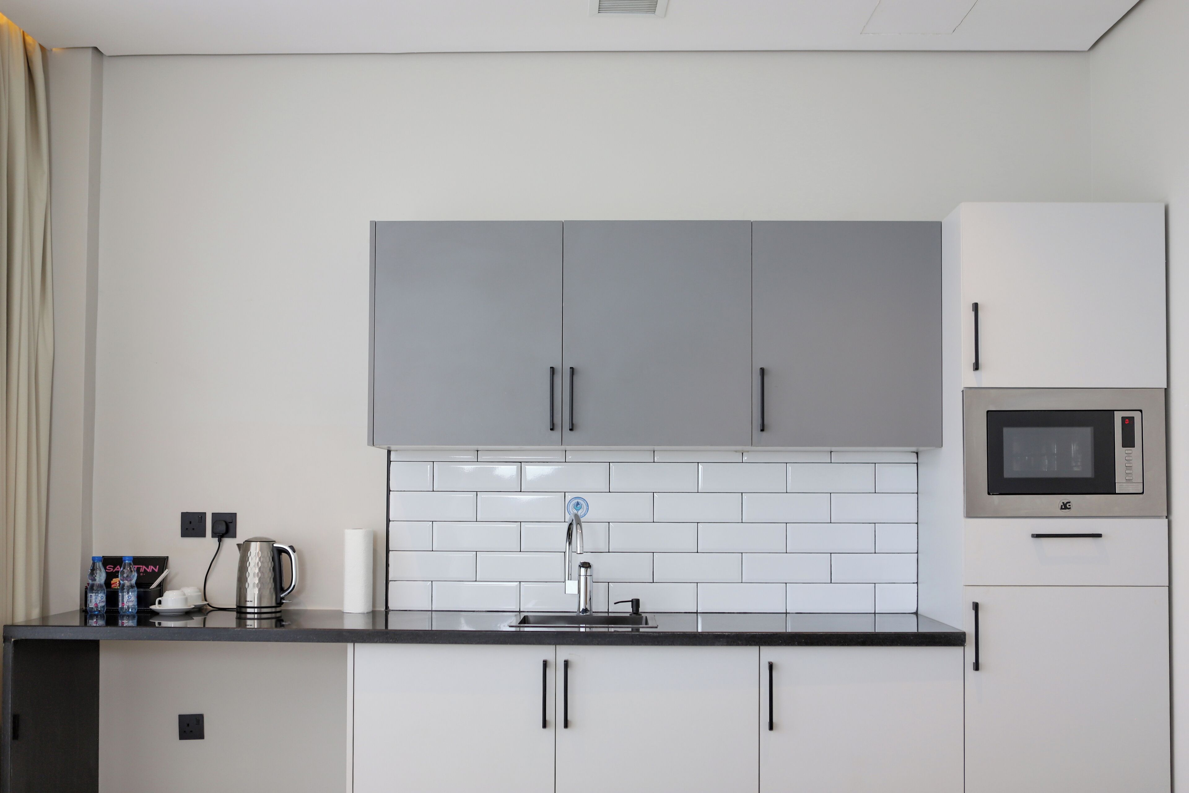 A modern kitchen with grey cabinets, a stainless steel sink, and a microwave.