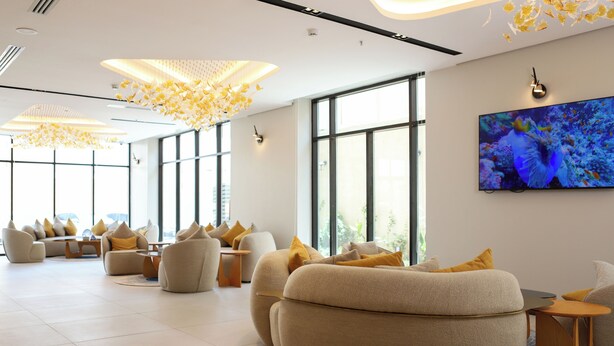 A modern lounge area with sofas and armchairs, a large window, and a wall-mounted TV. - Palm Core Hotel Al Rabwah (Riyadh)