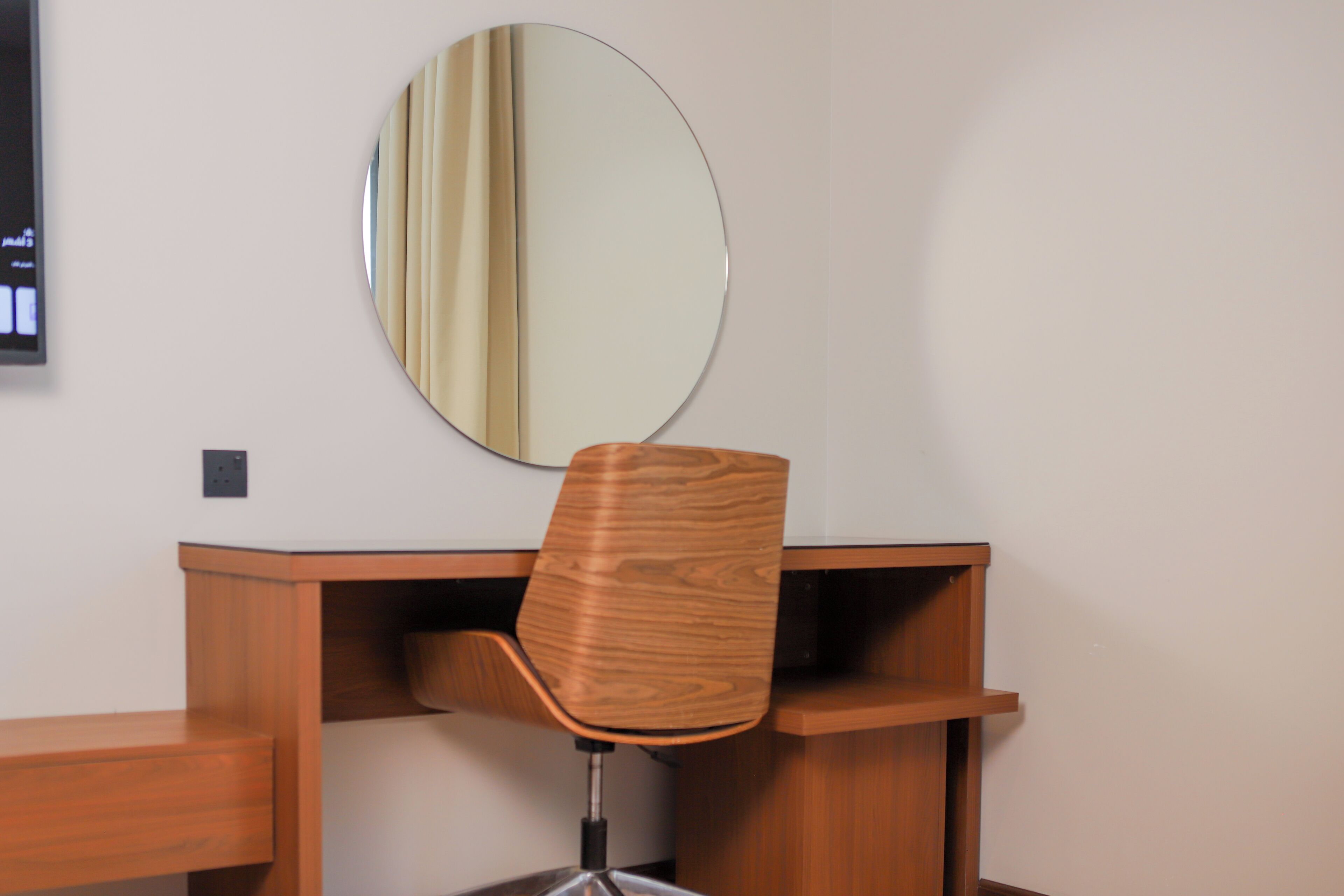 A wooden desk with a chair and a round mirror on the wall.