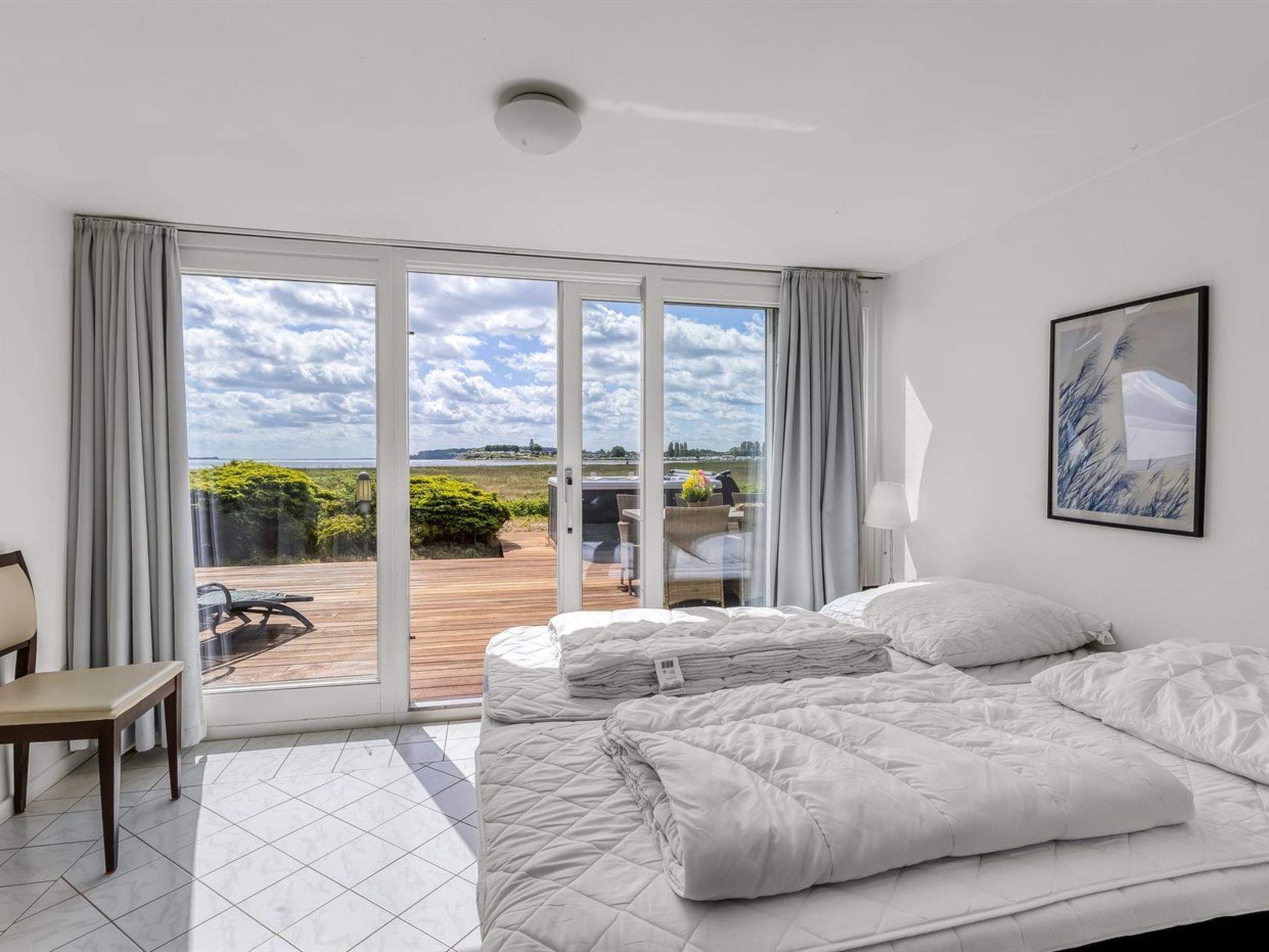 A bedroom with a large bed, a chair, and a view of a deck and outdoor area.