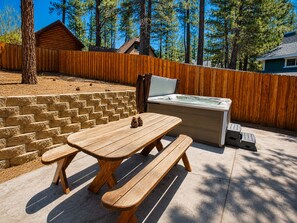 Ein Holztisch mit Bänken, einem Whirlpool und einer Steinmauer in einem Garten.