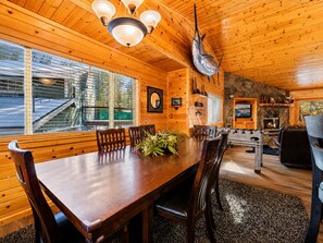 Ein Interieur einer Holzhütte mit einem Esstisch, Stühlen, einem Kamin und einem aufgehängten Fisch.