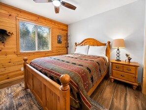 A wooden-paneled bedroom with a bed, a nightstand, a lamp, and a ceiling fan.