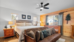 A bedroom with a bed, a wooden headboard, a ceiling fan, a nightstand, a dresser, and a window with curtains.