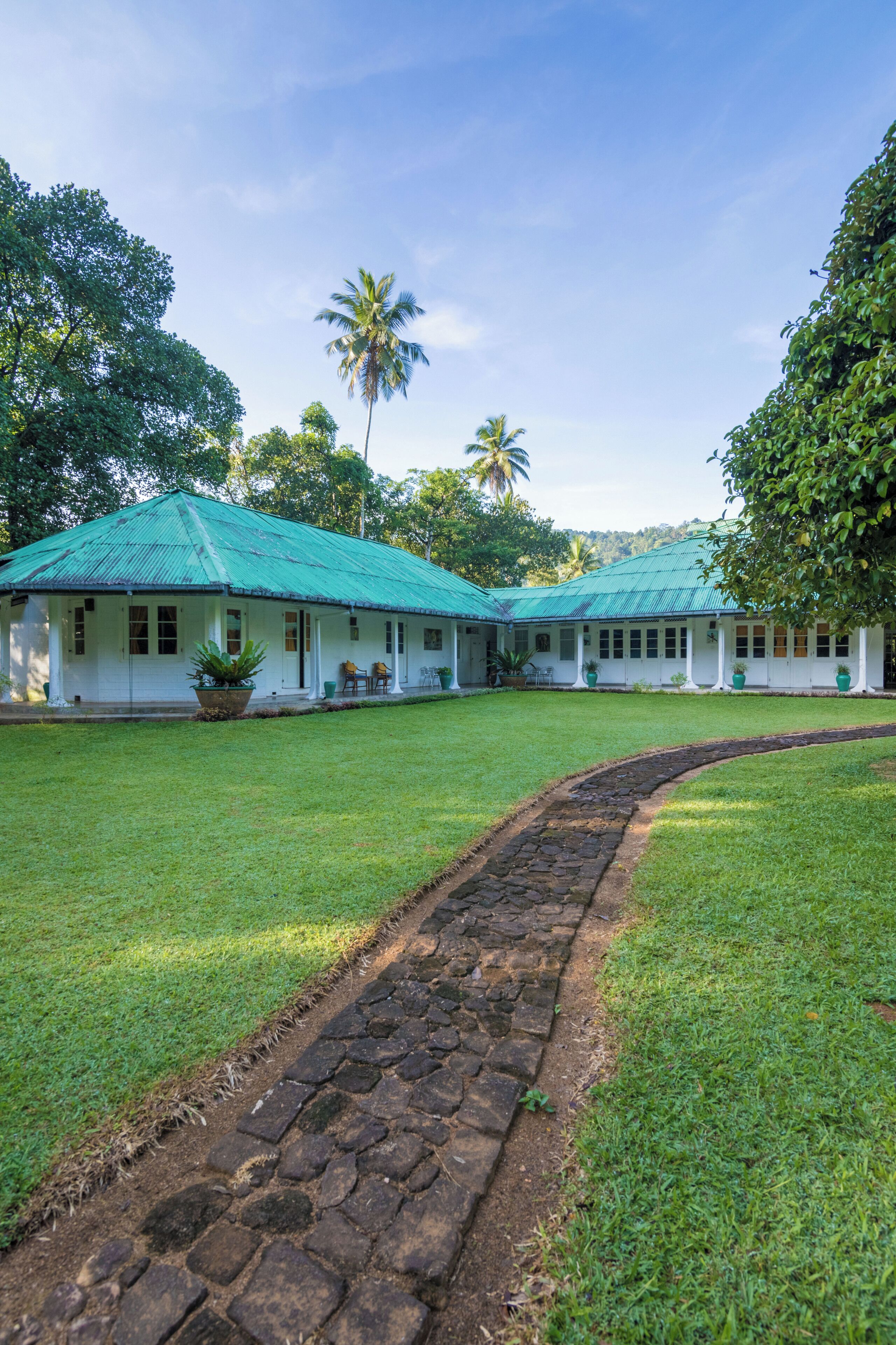 A white building with a green roof, surrounded by a well-maintained lawn and a stone pathway.