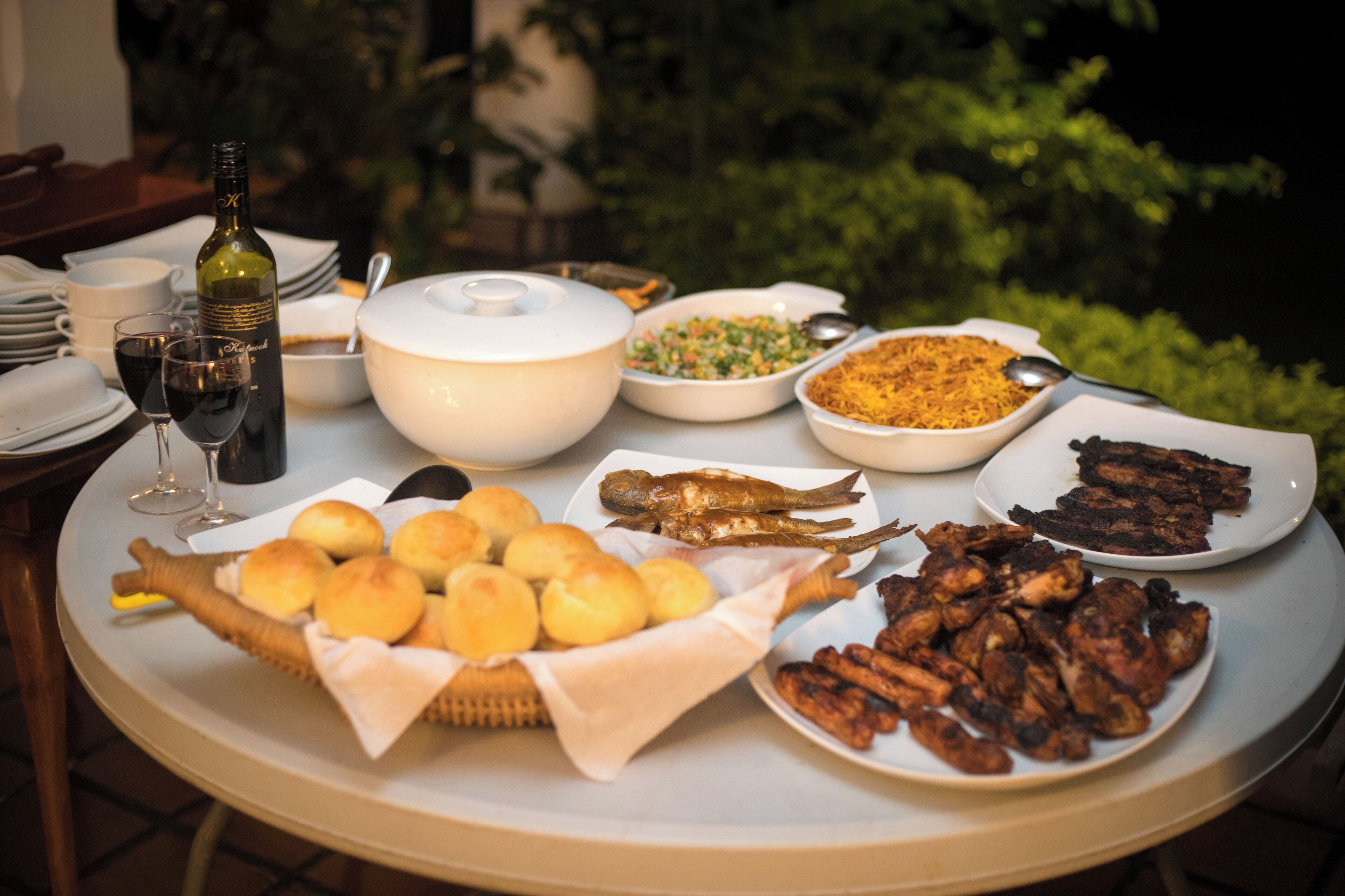 A table with various dishes, a bottle of wine, and a basket of rolls.