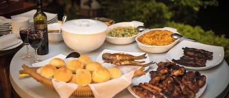 A table with various dishes, a bottle of wine, and a basket of rolls.