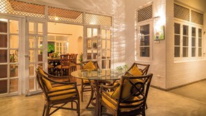Un coin repas avec des chaises en osier et une table en verre, une porte en bois avec des panneaux de verre et un luminaire fixé au mur.