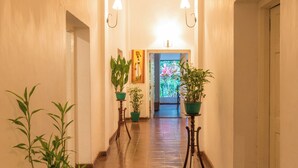 Un couloir doté d’un sol carrelé, de plantes en pot, de lampes fixées au mur et d’une œuvre d’art encadrée accrochée au mur.