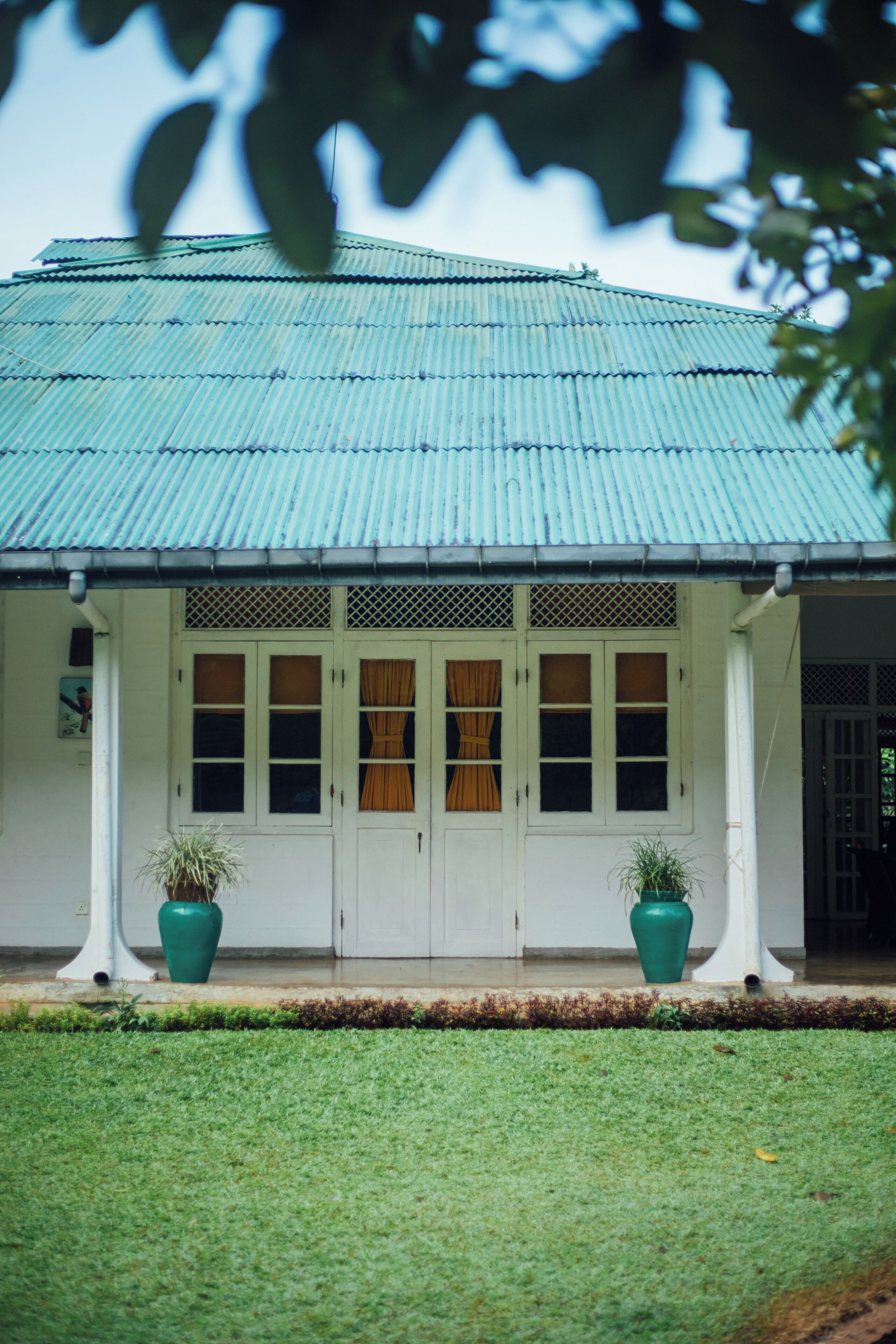 A building with a corrugated metal roof, white walls, and a small front porch with two potted plants.