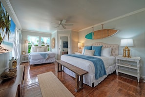 A bedroom with a bed, a bench, a surfboard, and a window with a view.
