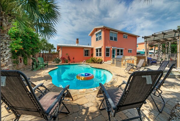 A backyard with a swimming pool, lounge chairs, and a two-story building.
