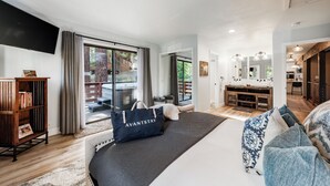 Un dormitorio amplio con una cama grande, una estantería, un televisor de pantalla plana y vistas al exterior a través de una puerta corrediza de vidrio.