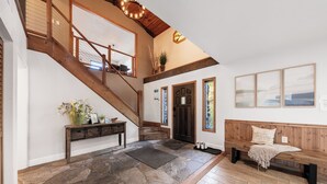 Un vestíbulo amplio con una escalera de madera, suelo de piedra, un banco y un banco con cojín.