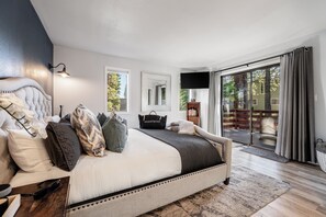 Un dormitorio con una cama grande, un televisor de pantalla plana, una puerta corrediza al balcón y vistas a árboles.