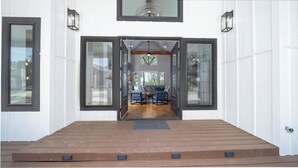 Eine Holzterrasse mit einer Bank und zwei Stühlen, einem Sofa und einem Esstisch im Hintergrund.