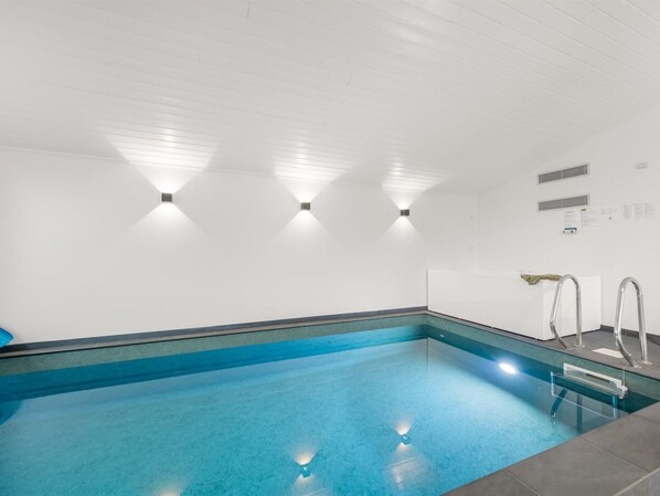 A swimming pool with clear blue water, surrounded by white walls and a tiled floor.