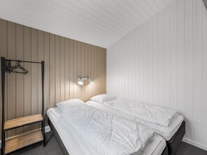 A bedroom with two beds, a bench, and a wall-mounted light fixture.