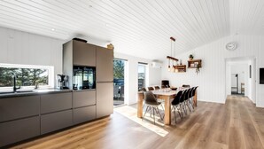 A modern kitchen with a large island, a dining area with a wooden table and chairs, and a white ceiling with linear paneling. - "Agnes" - 900m from the sea by Interhome (Ringkøbing)