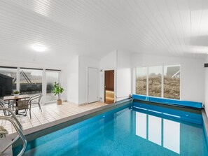 A modern indoor swimming pool with clear glass walls, a tiled floor, and a seating area with chairs and a table. - "Agnes" - 900m from the sea by Interhome (Ringkøbing)