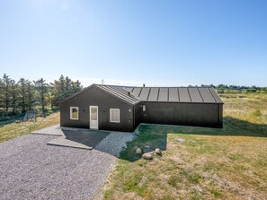 A modern building with a sloped roof, a gravel driveway, and a grassy area with rocks.