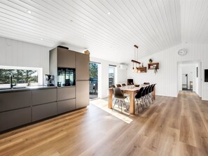 A modern kitchen with a central island, a dining area with a wooden table and chairs, and a large window providing a view of the outdoors. - "Agnes" - 900m from the sea by Interhome (Ringkøbing)