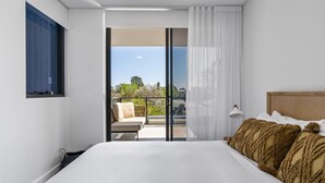 Ein Hotelzimmer mit einem großen Bett, einem Balkon mit Sitzgelegenheit und Blick auf Bäume und Gebäude.