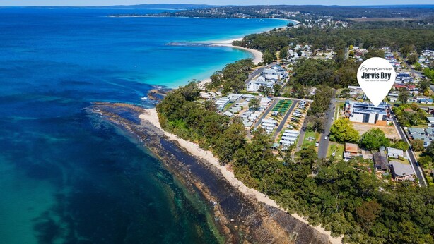 Ein Luftbild von Jervis Bay mit einer Küstenstraße, Strand und Campingplätzen.