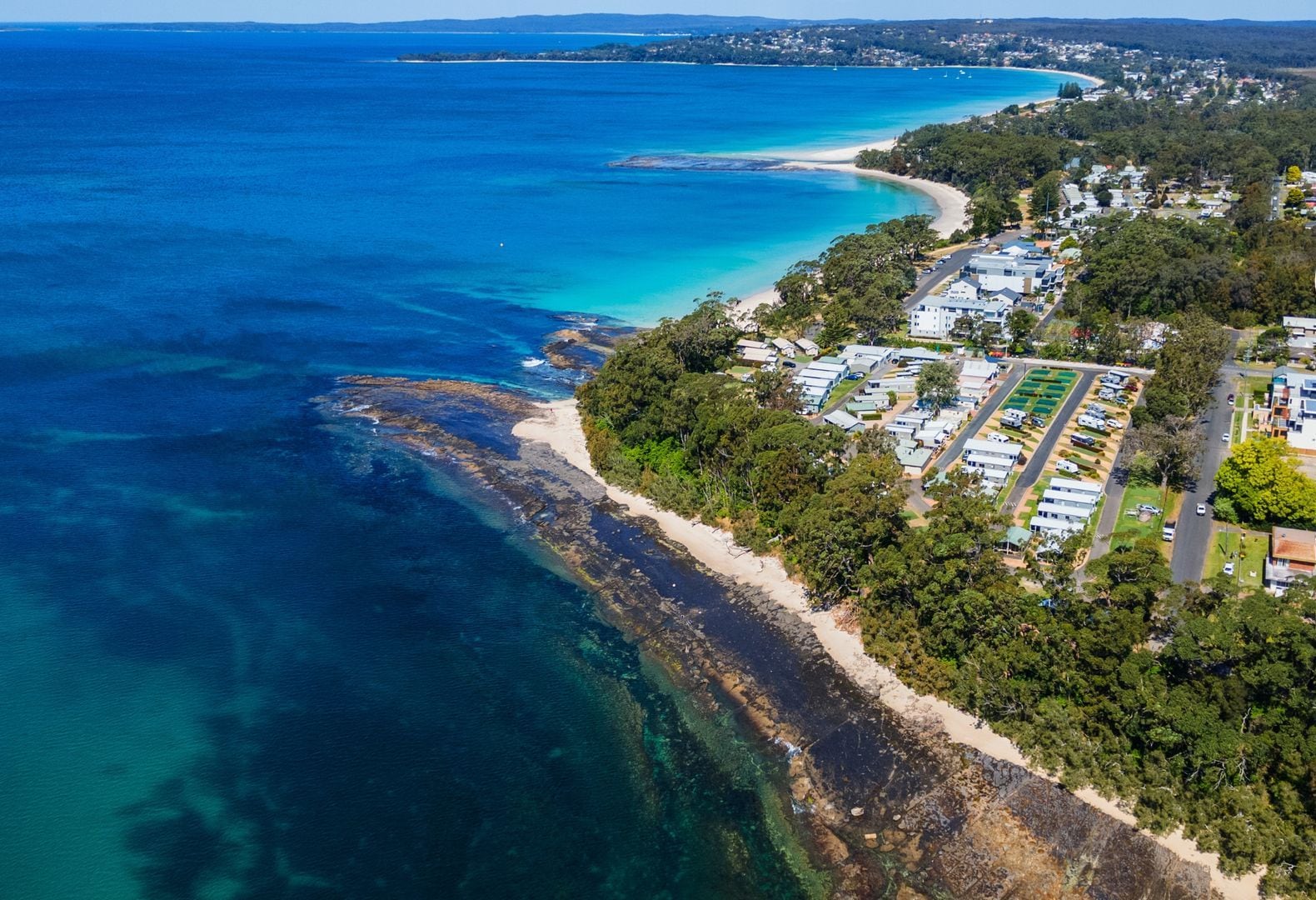 Ein Luftbild von Jervis Bay mit einer Küstenstraße, Strand und Campingplätzen.